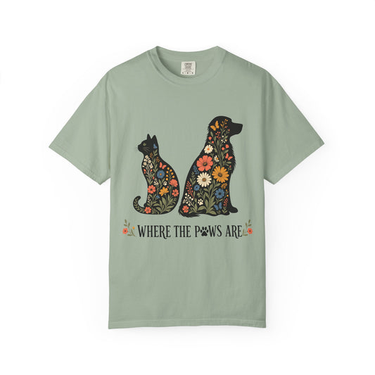 A sage green short-sleeve t-shirt with a graphic of a cat and dog filled with colorful flowers, above the text 'WHERE THE PAWS ARE'.