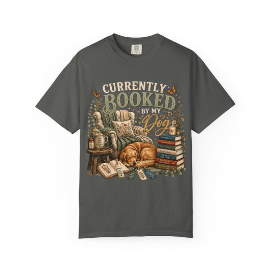 A dark gray crewneck t-shirt featuring a vintage-style graphic print of a cozy reading scene with a golden retriever dog, books, and the text 'CURRENTLY BOOKED BY MY Dog'.