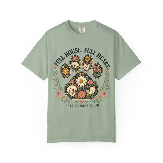 A sage green short-sleeve t-shirt with a colorful graphic of a dog paw print decorated with flowers and cartoon dogs, accompanied by the text 'FULL HOUSE, FULL HEART' and 'PET PARENT CLUB'.