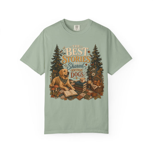 A sage green short-sleeve t-shirt with a detailed graphic on the front showing a golden retriever dog, books, a basket, and pine trees with the text 'THE BEST STORIES Shared WITH MY DOGS'.