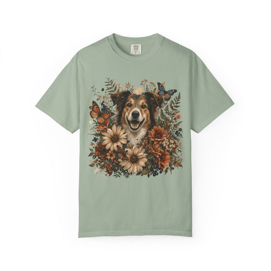 A sage green short-sleeve t-shirt featuring a detailed graphic print of a smiling dog surrounded by autumn flowers and butterflies, displayed on a clean white background.