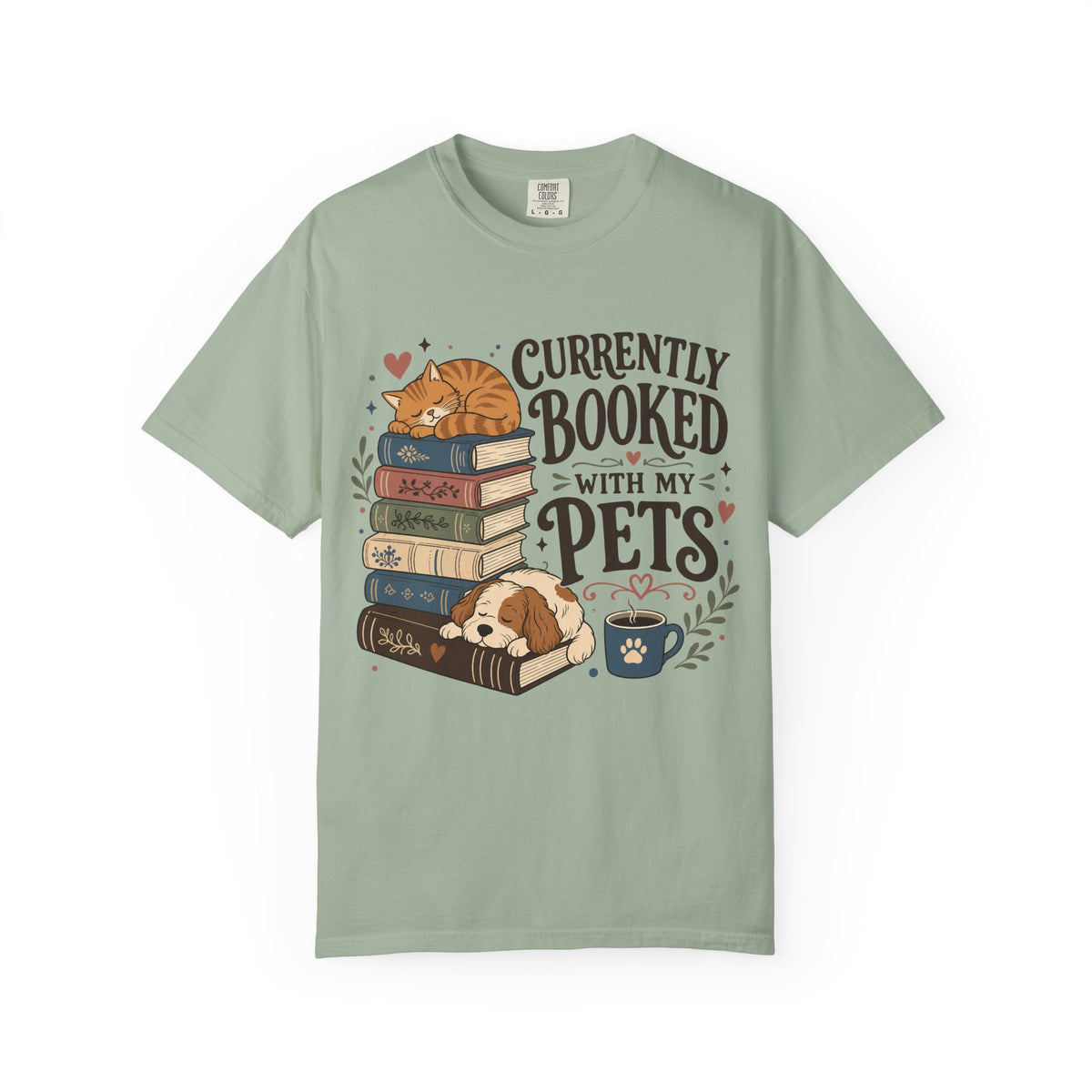 A sage green short-sleeve t-shirt with a graphic print of a cat on a stack of books, a sleeping puppy, a coffee cup, and the text 'CURRENTLY BOOKED WITH MY PETS'.