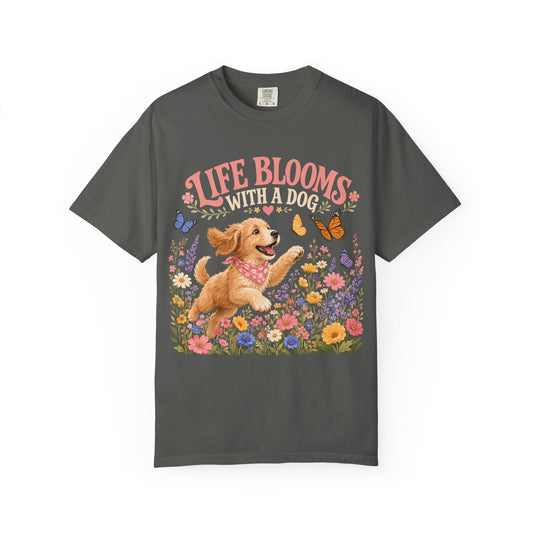 A dark gray crewneck t-shirt featuring a colorful graphic print of a golden retriever dog jumping in a field of flowers, with the text 'LIFE BLOOMS WITH A DOG' above it.