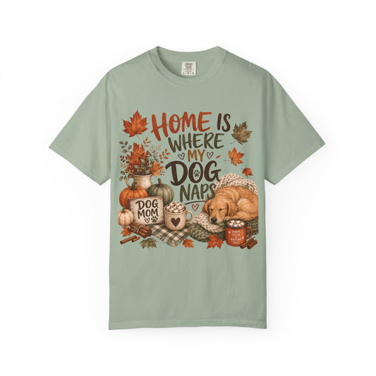 A sage green short-sleeve t-shirt with a detailed autumn-themed graphic on the front. The graphic features the text 'HOME IS WHERE MY DOG NAPS' in stylized lettering, surrounded by fall elements like pumpkins, maple leaves, a cozy mug, and a golden retriever dog illustration.