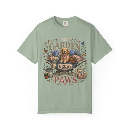 A sage green short-sleeve t-shirt with a detailed graphic print on the front. The graphic features a golden retriever dog sitting in a wheelbarrow surrounded by flowers and the text 'MY GARDEN GROWS BETTER WITH PAWS'.