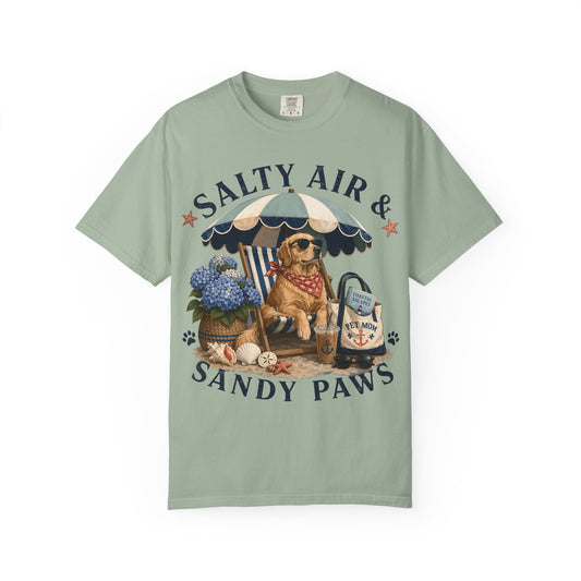 A sage green short-sleeve t-shirt with a detailed graphic print of a dog at a beach under a striped umbrella, featuring the text 'SALTY AIR & SANDY PAWS'.