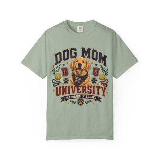 A sage green short-sleeve t-shirt with a 'Dog Mom University' graphic featuring a golden retriever dog and decorative elements, displayed on a clean white background.
