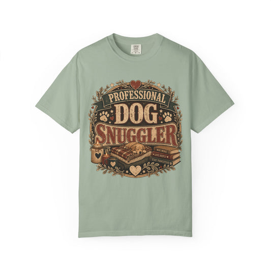 A sage green short-sleeve t-shirt with a vintage-style graphic on the front that reads 'PROFESSIONAL DOG SNUGGLER' in brown and beige tones, featuring a dog, leash, and paw prints.