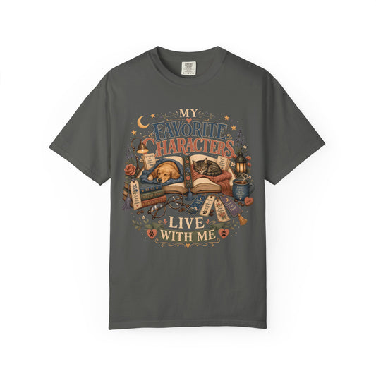 A dark gray crewneck t-shirt featuring a detailed graphic print on the front. The graphic depicts a cozy scene with a sleeping cat under an open book, surrounded by magical elements like a cauldron, potion bottle, scrolls, and stars, with the text 'MY FAVORITE CHARACTERS LIVE WITH ME'.